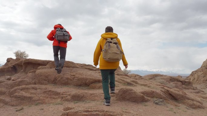 两个旅行者沿着野生岩石区向前走，爬上了山
