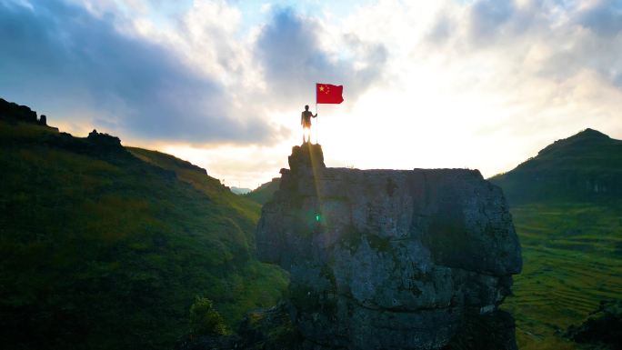 五星红旗迎风飘扬青年山顶举起红旗逆光背影