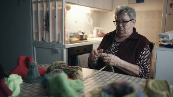 肥胖老年妇女坐在桌边一边自言自语一边在家织毛衣