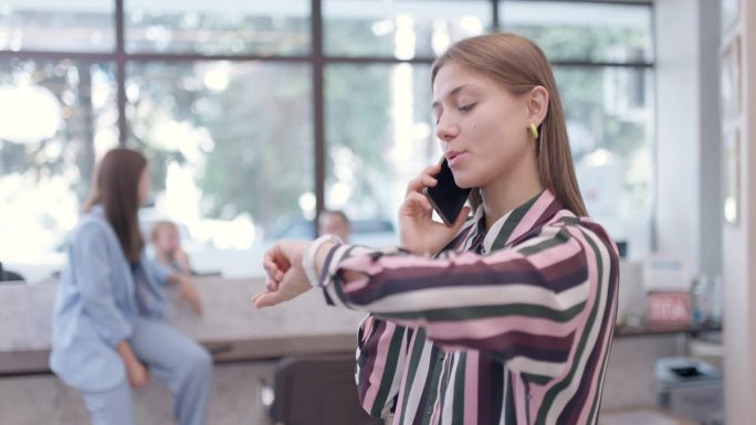 年轻的女商人在办公室里打电话，查看手表上的时间，结束通话，看着相机。