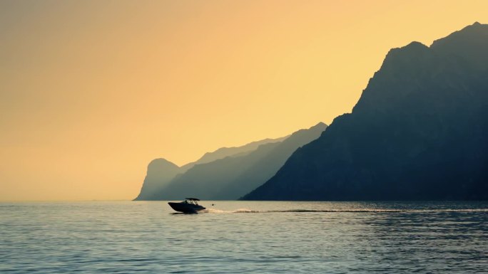 沿着剪影山脉和日落时的橙色天空，加尔达湖上的SLO MO摩托艇