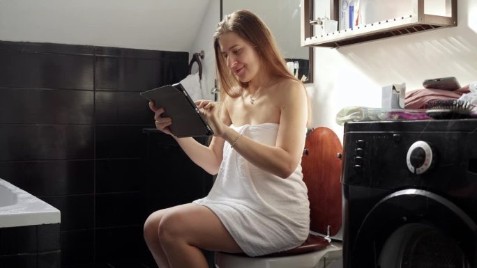 一个坐在马桶上使用平板电脑的女人。远程工作，教育，勤奋的概念