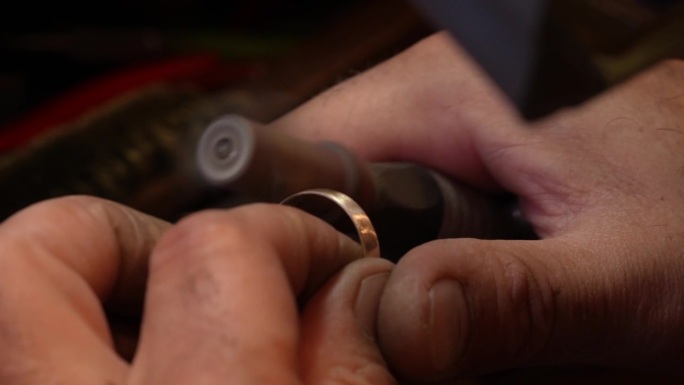 在手工制作金戒指的过程中，珠宝商使用安装在柔性轴钻机上的砂纸卷来打磨金属