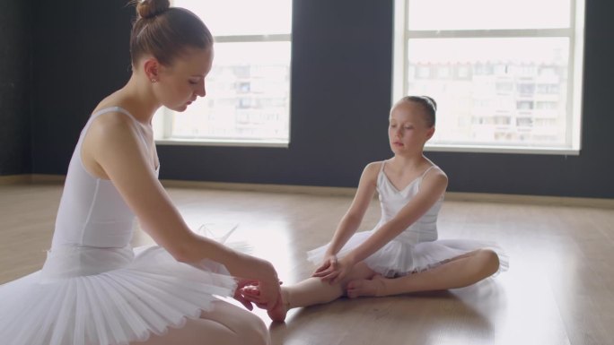 芭蕾舞演员在芭蕾舞课上伸展女孩的脚踝