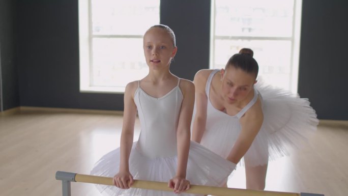 女孩在芭蕾课上把腿放在扶手上伸展