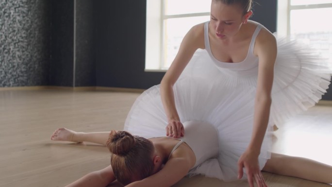 小芭蕾舞者身体向地板倾斜，老师在后面