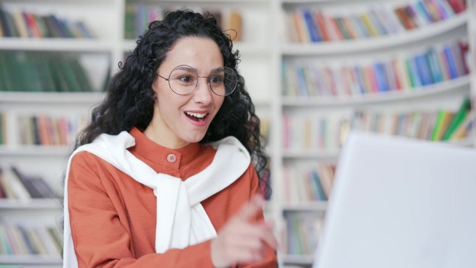 在校园图书馆用笔记本电脑工作时，一位快乐的女学生在灵感迸发的瞬间竖起了食指