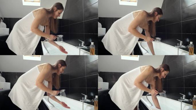 穿着白毛巾的年轻女子正在检查水温并往浴缸里注水。保健、卫生和日常生活的概念。