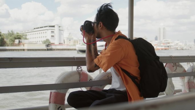 年轻的亚洲男性游客乘坐轮渡游览，并在轮渡上拍照。