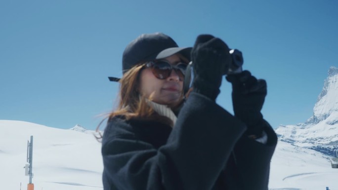 年轻女子在雪山上用数码相机拍照。