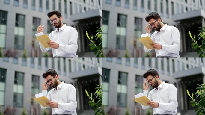 一个穿着白衬衫的失望的年轻人站在办公楼附近的街道上读着一封带有坏消息的信
