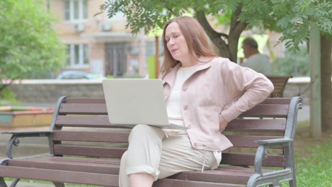 现代老年妇女与背部疼痛使用笔记本电脑户外