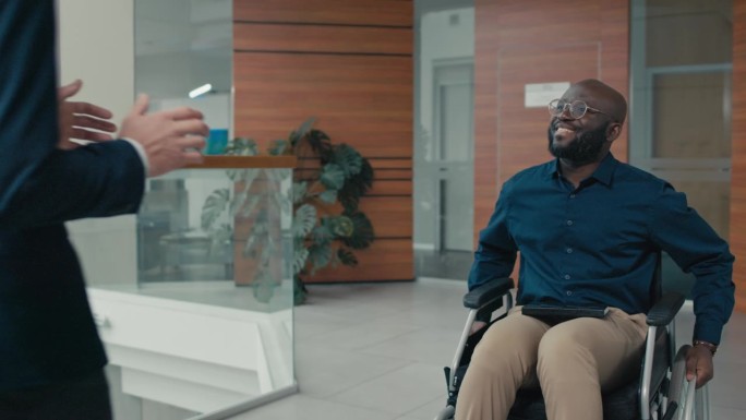 坐在轮椅上的快乐男子向办公室的同事打招呼