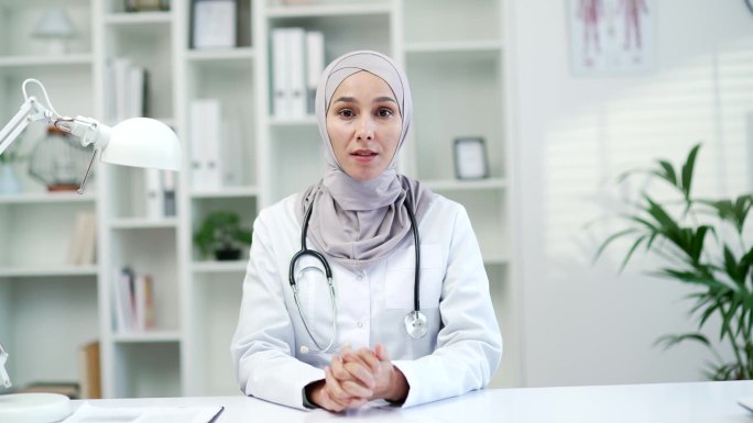 在医院的诊所里，自信的穆斯林女医生看着摄像头，听着病人的视频通话。