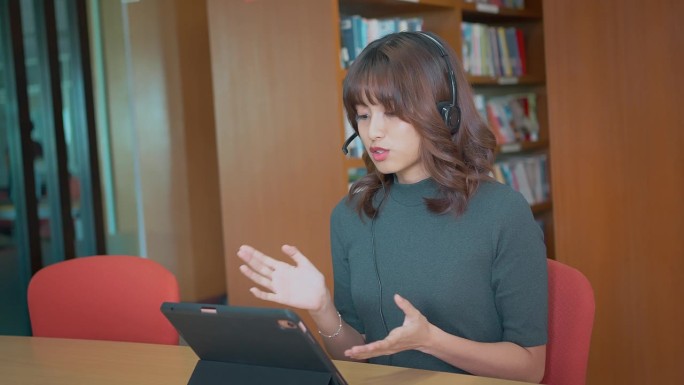 年轻的亚洲女子学校的大学生戴着耳机学习观看在线网络研讨会网络广播类看数字平板电脑电子学习远程课程或视