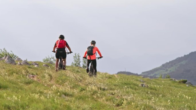 两个女人在阳光明媚的山上骑着电动山地车