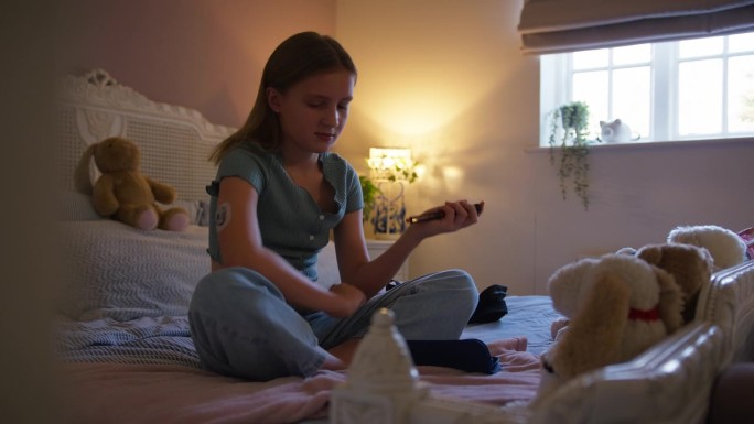 年轻的糖尿病女孩坐在家里卧室的床上，使用测量和检查胰岛素水平的工具