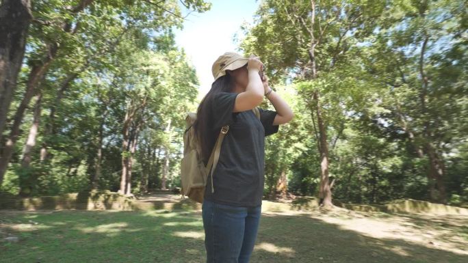 徒步旅行者迷人的快乐的年轻女孩背着背包在绿色的树林里徒步旅行