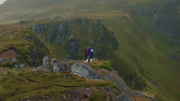 鸟瞰图，年轻的旅行者家庭和一只白狗站在悬崖顶上，看着下面史诗般的北欧景色