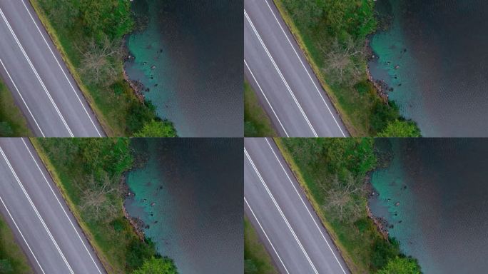 修复湖岸与岩石和蓝藻蓝藻和道路的对角线顶部镜头。汽车沿着马路行驶。绿草如茵，绿树成荫的路和水体之间。