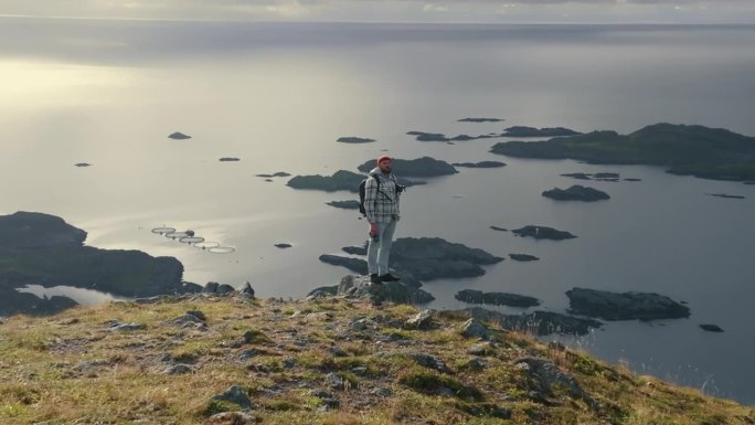 360度无人机拍摄的一个年轻男性背包客站在峡湾顶部，观看挪威海岛屿的壮丽景色