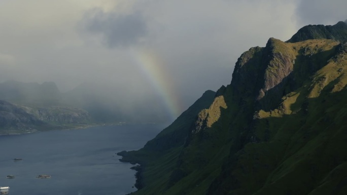 无人机飞过岩石峡湾，在水面上的云层中露出彩虹