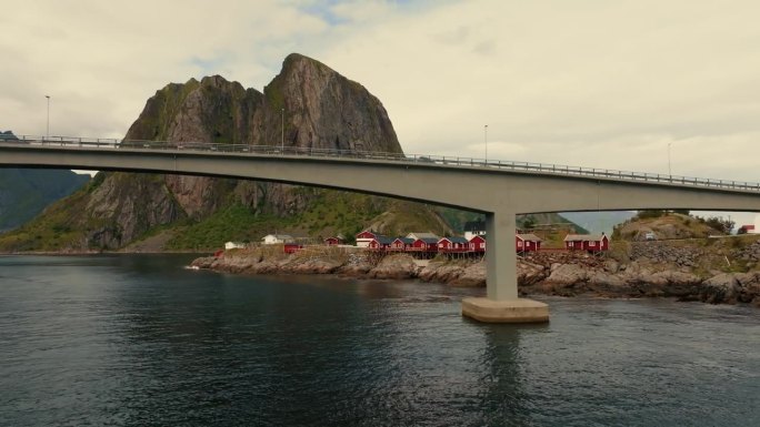 无人机在公路桥下飞行，揭示了位于岩石岸边的传统红色rorbu房屋