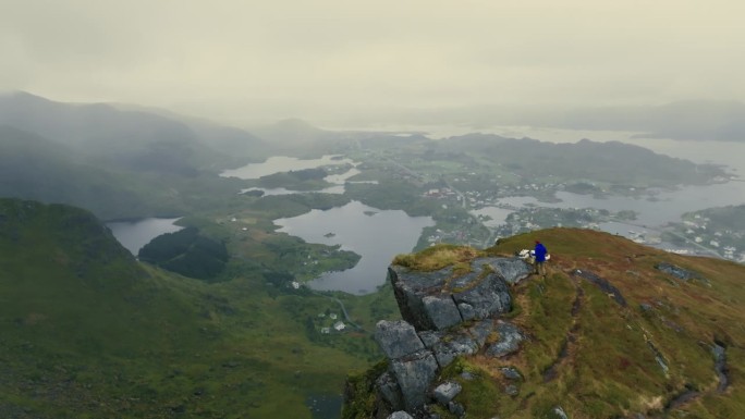 一名男性旅行者带着一只白狗徒步到山顶，观察令人惊叹的北欧景观