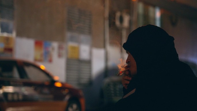 男人在街边抽烟蹲守过路的行人