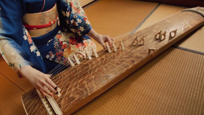 日本传统音乐会表演特写。穿着和服的匿名女音乐家，演奏古典琴。一个女人熟练地使用绳子的高角度镜头