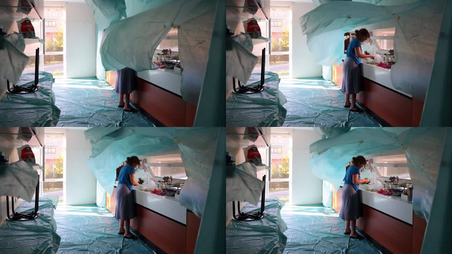 在粉刷过的房子的厨房里，一个家庭主妇正试图在飘动的尼龙薄布中做饭。