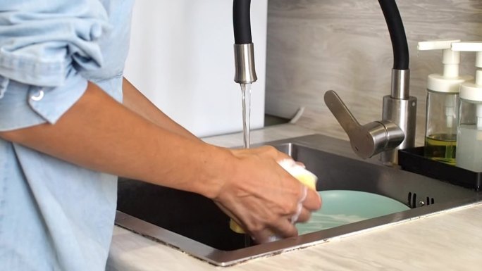 在现代厨房里，一名妇女将洗洁精挤在黄色海绵上