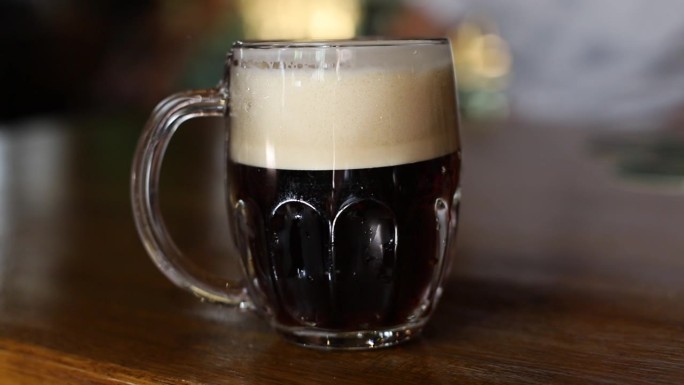 在酒吧的木桌上，用传统的马克杯盛着泡沫头的冰镇黑啤酒