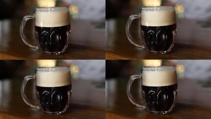 在酒吧的木桌上，用传统的马克杯盛着泡沫头的冰镇黑啤酒