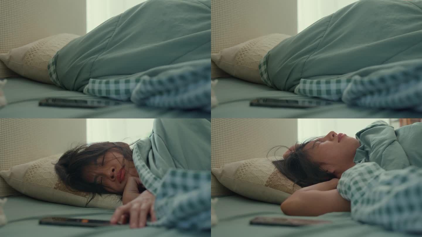 年轻的亚洲女人穿着睡衣，躺在方便舒适的床上，早上醒来时睡眼朦胧，感觉手机闹铃嘈杂，在家里的卧室里叫醒