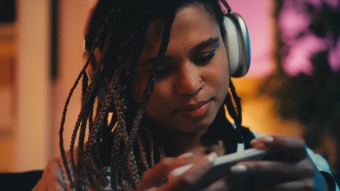 快乐的年轻女子戴着耳机在智能手机上玩电子游戏，业余爱好，休息