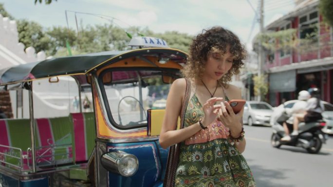 美丽的年轻女子喜欢旅行，喜欢用智能手机自拍。背景是一辆泰国的嘟嘟车。
