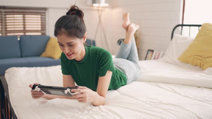 快乐与放松:年轻女性在卧室的床上玩电子游戏时微笑