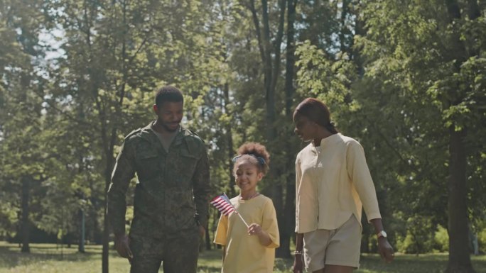 女孩手持美国国旗，与身穿军装的父亲和母亲同行