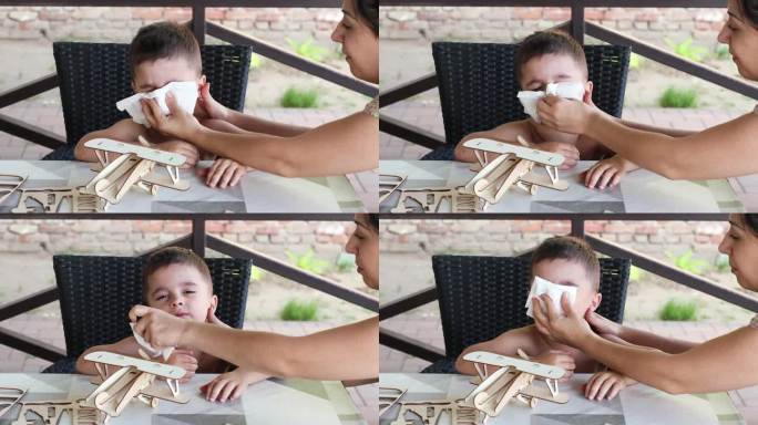 小男孩在妈妈的帮助下打喷嚏或擤鼻涕。皱鼻子，眯眼睛，家里生病的孩子。流感，流鼻涕，病毒或过敏的概念。