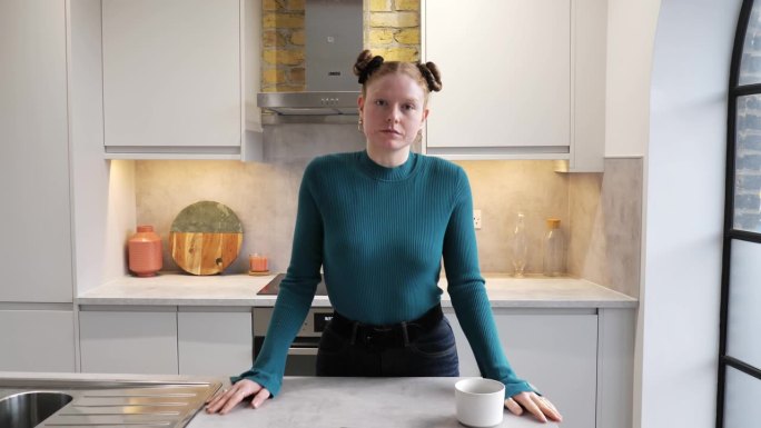 红发女人站在厨房柜台后面看着摄像机，4k视频