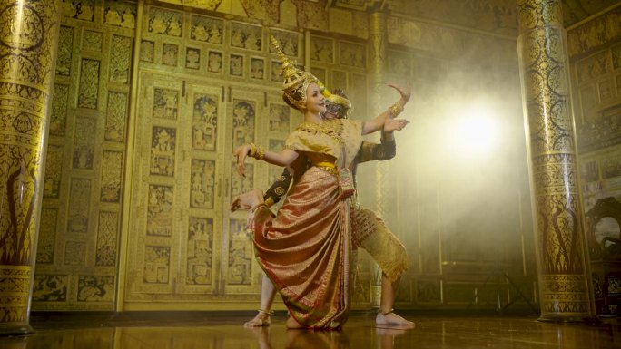 侧视图美丽的亚洲妇女穿着泰国传统服装，与泰国经典舞蹈动作一起跳舞，从拉玛金面具黑猴子与泰国绘画在公共