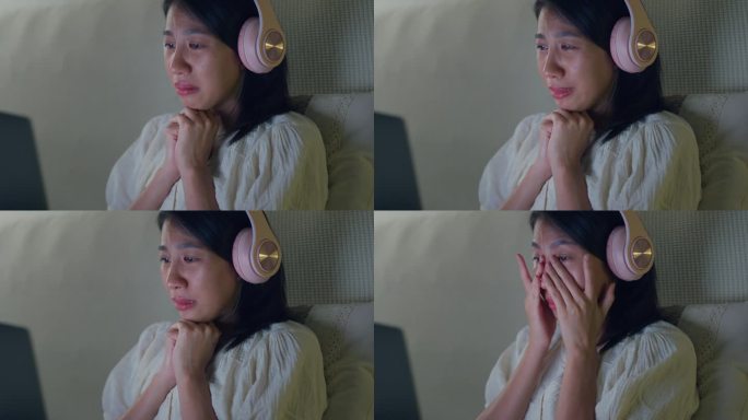 年轻的亚洲女孩的特写媒体上瘾在床上戴着耳机哭在流媒体观看最喜欢的电影在线视频点播，视频点播在家里晚上