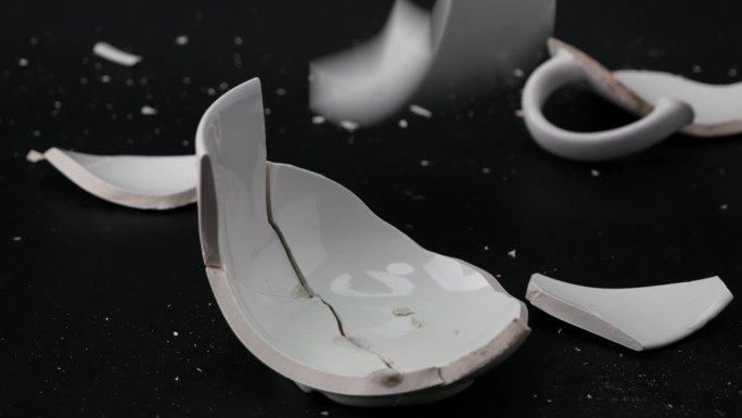 破碎的白色茶杯或汤在黑色的背景孤立。近距离观察破碎的陶瓷杯。象征离婚或损失