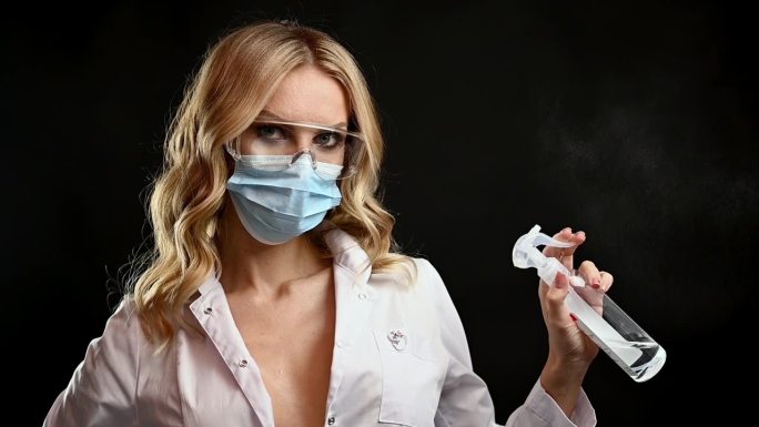 年轻的商务女员工戴着面部防护医用口罩，将瓶子里的抗菌消毒凝胶涂在手上，开始在现代办公室里使用电脑，预