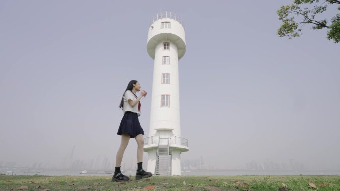 女生从武昌江滩小垦丁江边的白色灯塔前走过