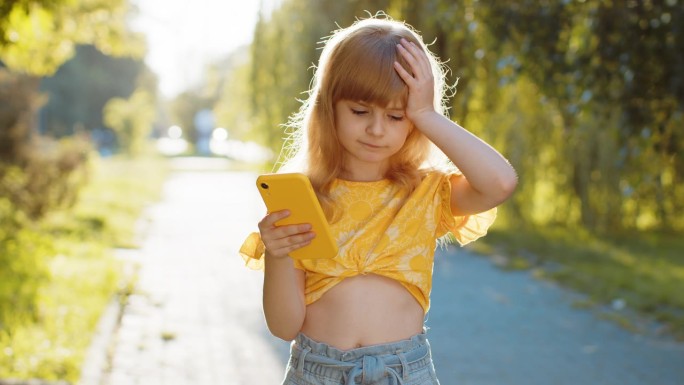 意外的孩子女孩玩游戏用智能手机输了，坏消息，财富损失失败在城市公园街道