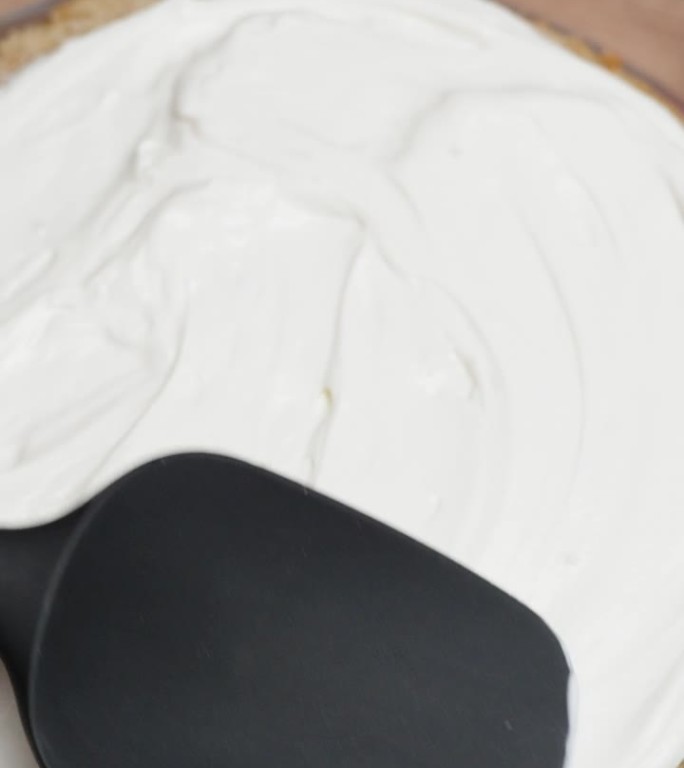 从上面看，糕点师正在把白奶油涂在蛋糕层上。垂直视频。