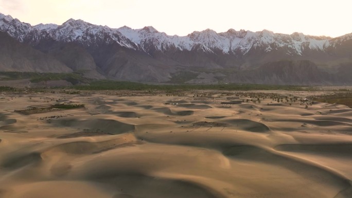 从巴基斯坦北部斯卡都的喀喇昆仑山脉拍摄的被雪帽山包围的卡特帕纳寒冷沙漠的无人机日落视图