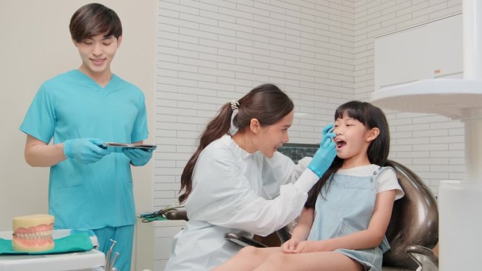 一位亚洲女牙医在牙科诊所为一位女孩检查牙齿。